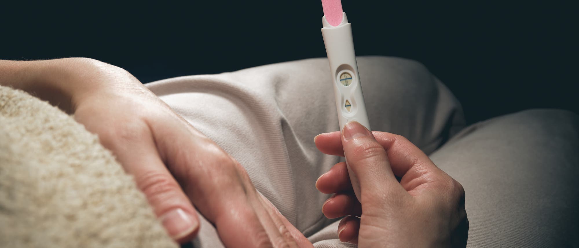 Eine Frau hält einen positiven Schwangerschaftstest in der Hand. Mit der anderen Hand hält sie sich den Bauch. Eine Frau hält einen positiven Schwangerschaftstest in der Hand. Mit der anderen Hand hält sie sich den Bauch.